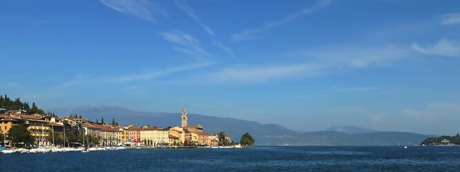 Trip Reisen beliebte Urlaubsziele am Gardasee -  Mit einer Fläche von 370 km² ist der Gardasee der größte See Italiens. Es liegt am Fuße der Alpen und erstreckt sich über drei Staaten: Lombardei, Venetien und Trentino. Die maximale Tiefe des Sees beträgt 346 m, er hat eine längliche Form und sein nördliches Ende ist sehr schmal. Dort ist der See von den Bergen der Gruppo di Baldo umgeben. Du trittst aus deinem gemütlichen Hotelzimmer und es begrüßt dich die warme italienische Sonne. Du blickst auf den atemberaubenden Gardasee, der in zahlreichen Blautönen schimmert - von tiefem Dunkelblau bis zu funkelndem Türkis. Majestätische Berge umgeben dich, während die Brise sanft deine Haut streichelt und der Duft von blühenden Zitronenbäumen deine Nase kitzelt. Du schlenderst die malerischen, engen Gassen entlang, vorbei an farbenfrohen, blumengeschmückten Häusern. Vereinzelt unterbricht das fröhliche Lachen der Einheimischen die friedvolle Stille. Du fühlst dich wie in einem Traum, der nicht enden will. Jeder Schritt führt dich zu neuen Entdeckungen und Abenteuern. Du probierst die köstliche italienische Küche mit ihren frischen Zutaten und verführerischen Aromen. Die Sonne geht langsam unter und taucht den Himmel in ein leuchtendes Orange-rot - ein spektakulärer Anblick.